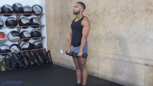 A Man Is Holding A Pair Of Dumbbells In Front Of A Wall With Balls On It GIF