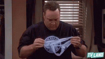 A Man Is Holding A Pair Of Underwear In His Hands In A Room . GIF