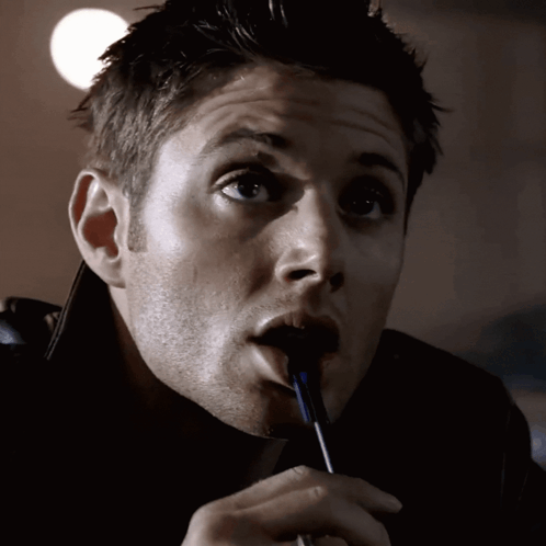 A Man Is Holding A Pen In His Mouth And Looking At The Camera GIF