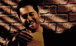 A Man Is Holding A Piece Of Paper In Front Of A Brick Wall And Smiling . GIF