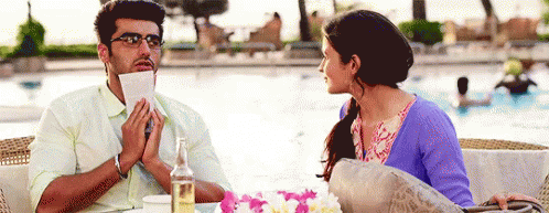 A Man Is Holding A Piece Of Paper In His Mouth And A Woman Is Looking At Him GIF