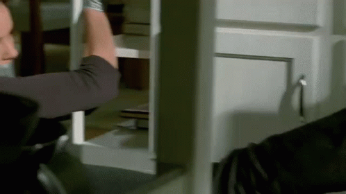 A Man Is Holding A Piece Of Wood In His Hand While Standing In Front Of A Cabinet . GIF