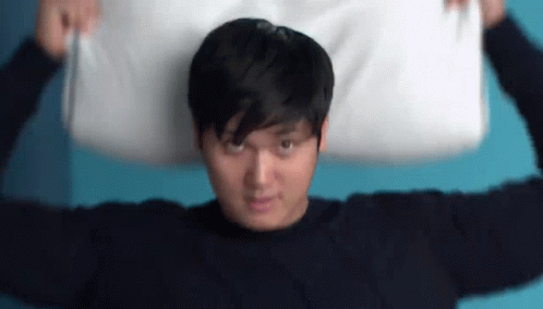 A Man Is Holding A Pillow Over His Head . GIF
