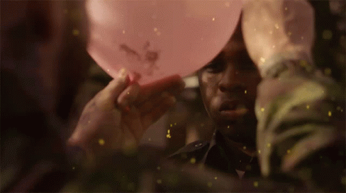 A Man Is Holding A Pink Balloon Over His Head With Flowers On It GIF