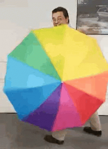 A Man Is Holding A Rainbow Colored Umbrella In Front Of Him GIF