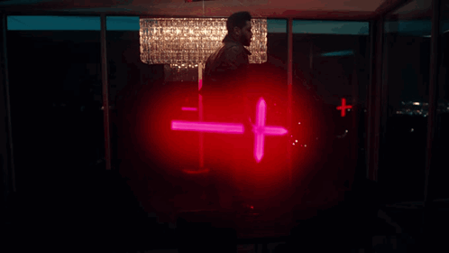 A Man Is Holding A Red Cross In Front Of A Crystal Chandelier GIF