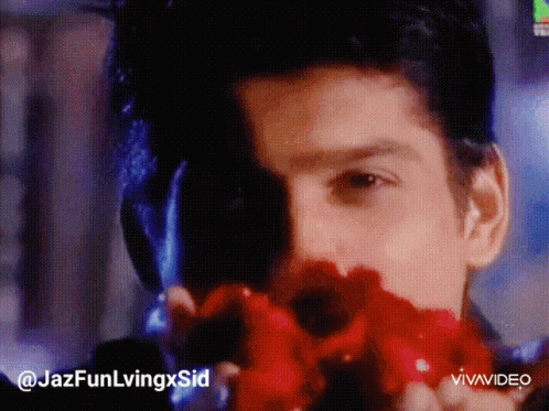 A Man Is Holding A Red Flower In Front Of His Face .. GIF