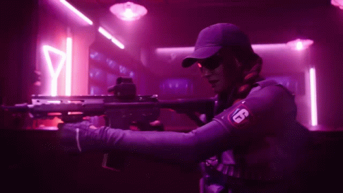 A Man Is Holding A Rifle In A Dark Room With Neon Lights . GIF