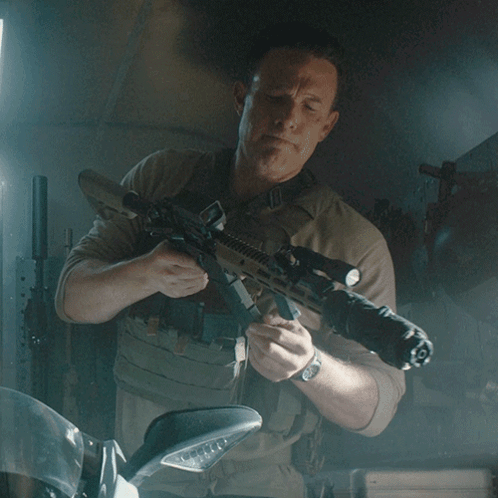 A Man Is Holding A Rifle With A Scope That Has The Letter O On It GIF