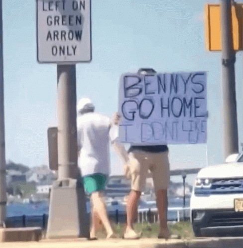 A Man Is Holding A Sign That Says Bennys Go Home GIF
