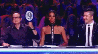 A Man Is Holding A Sign With The Number 9 On It While A Woman Looks On . GIF