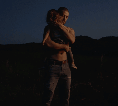 A Man Is Holding A Small Child In His Arms In The Dark GIF