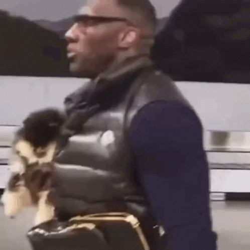 A Man Is Holding A Small Dog In His Arms While Walking Down The Street . GIF