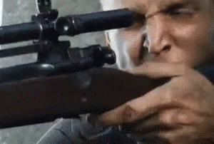 A Man Is Holding A Sniper Rifle In His Hand And Looking Through The Scope . GIF