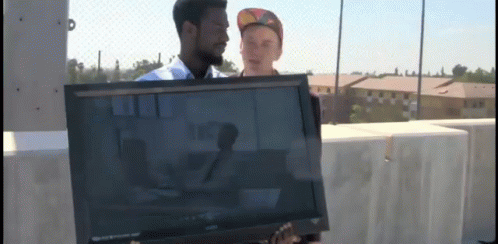 A Man Is Holding A Sony Television While Another Man Stands Behind Him GIF
