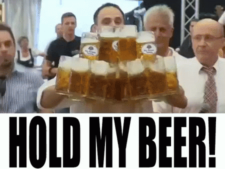A Man Is Holding A Stack Of Beer Mugs With The Words Hold My Beer Written Below Him GIF