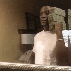 A Man Is Holding A Stack Of Money In His Hand In Front Of A Mirror . GIF
