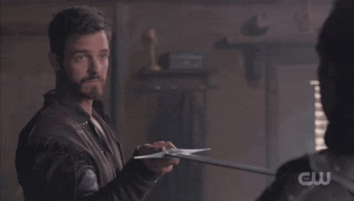 A Man Is Holding A Sword In Front Of Another Man With A Cw Logo Visible GIF