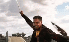 A Man Is Holding A Sword In The Air In A Field . GIF