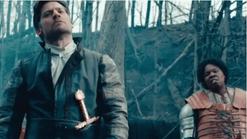 A Man Is Holding A Sword While Standing Next To Another Man . GIF