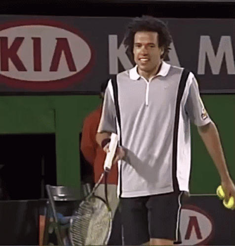 A Man Is Holding A Tennis Racquet And A Tennis Ball In Front Of A Kia Sign GIF