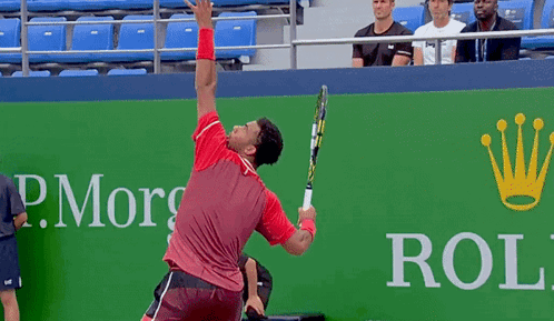 A Man Is Holding A Tennis Racquet In Front Of A Rolex Ad GIF