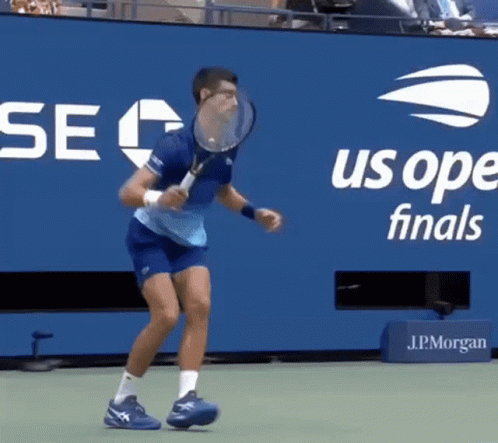 A Man Is Holding A Tennis Racquet In Front Of A Us Open Finals Banner GIF