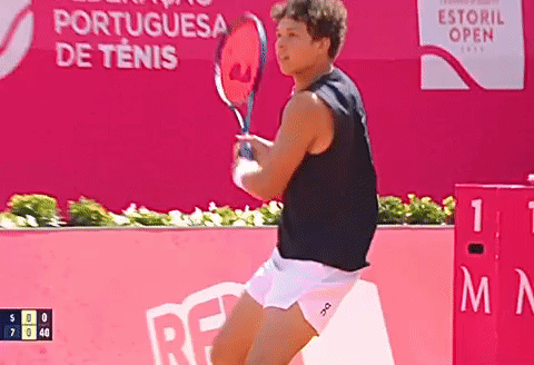 A Man Is Holding A Tennis Racquet In Front Of An Advertisement For The Portuguesa De Tenis GIF