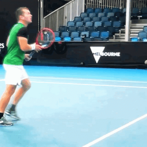 A Man Is Holding A Tennis Racquet On A Court With A Melbourne Sign Behind Him GIF