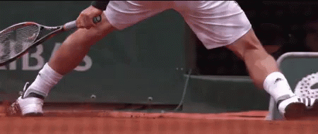 A Man Is Holding A Tennis Racquet On A Red Court GIF