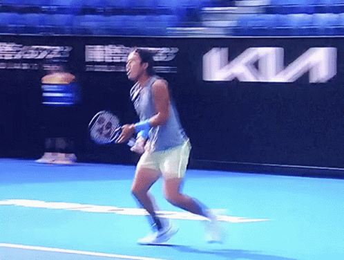 A Man Is Holding A Tennis Racquet On A Tennis Court In Front Of A Kia Ad GIF