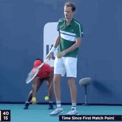 A Man Is Holding A Tennis Racquet On A Tennis Court While A Woman Stands Behind Him . GIF