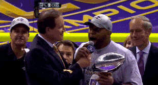 A Man Is Holding A Trophy And Talking Into A Microphone GIF