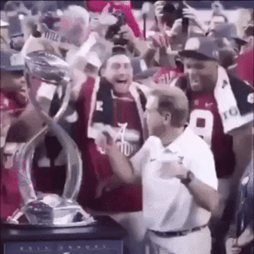 A Man Is Holding A Trophy In A Crowd Of People . GIF