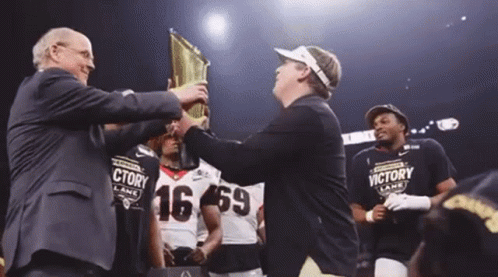 a man is holding a trophy in front of a group of football players wearing victory lane shirts