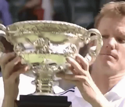A Man Is Holding A Trophy In His Hands And Looking At It . GIF