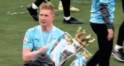 A Man Is Holding A Trophy On A Soccer Field . GIF