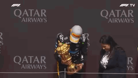 A Man Is Holding A Trophy On A Stage In Front Of A Qatar Airways Sign . GIF