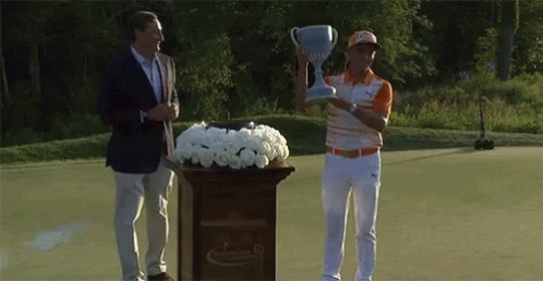 A Man Is Holding A Trophy While Standing Next To A Podium With Flowers GIF