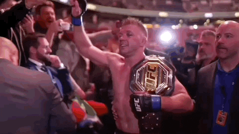 A Man Is Holding A Ufc Heavyweight Championship Belt In A Boxing Ring . GIF
