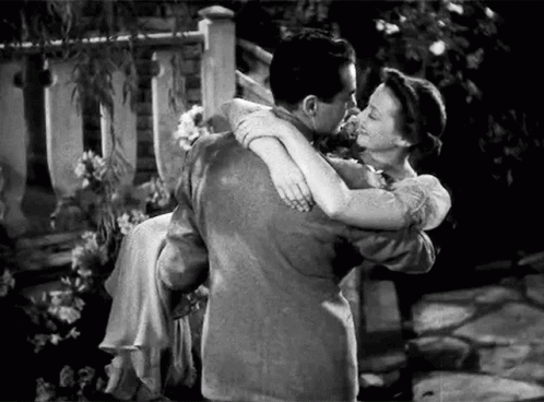 A Man Is Holding A Woman In His Arms And They Are Kissing . GIF