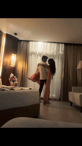 A Man Is Holding A Woman In His Arms In A Room GIF