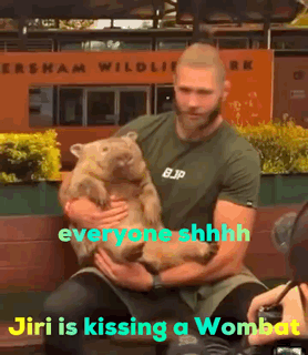 A Man Is Holding A Wombat In Front Of A Sign That Says ' Everyone Shhhh ' GIF