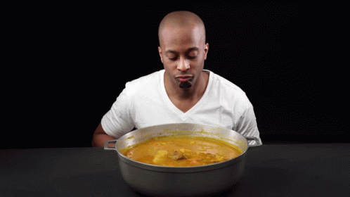 A Man Is Holding A Wooden Spoon In Front Of A Pot Of Soup GIF
