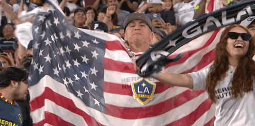 A Man Is Holding An American Flag And A Woman Is Wearing A Shirt That Says Herbalife GIF