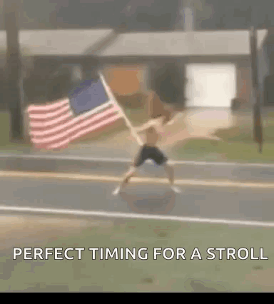 A Man Is Holding An American Flag On The Side Of The Road . GIF
