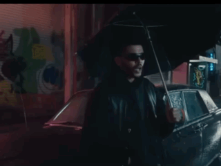 A Man Is Holding An Umbrella In Front Of A Car . GIF