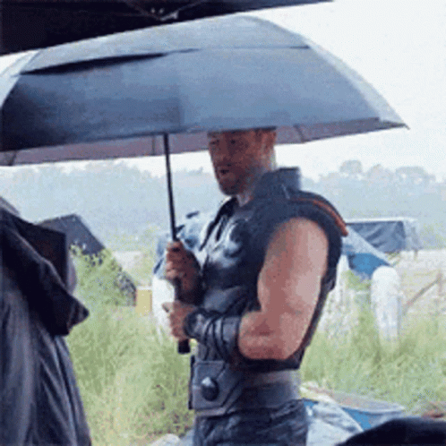 A Man Is Holding An Umbrella While Standing In The Rain GIF