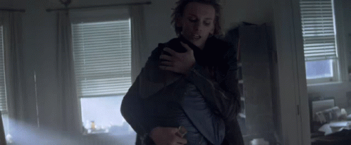 A Man Is Holding Another Man In His Arms In A Room With Blinds GIF