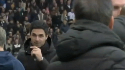 A Man Is Holding His Finger To His Nose While Standing In Front Of A Crowd . GIF
